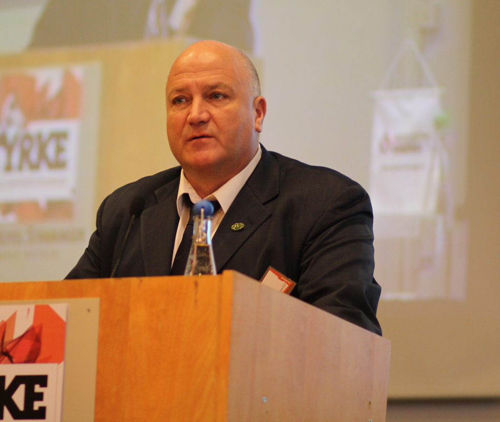 Bob Crow, wearing a suit with loosened tie, behind a lectern